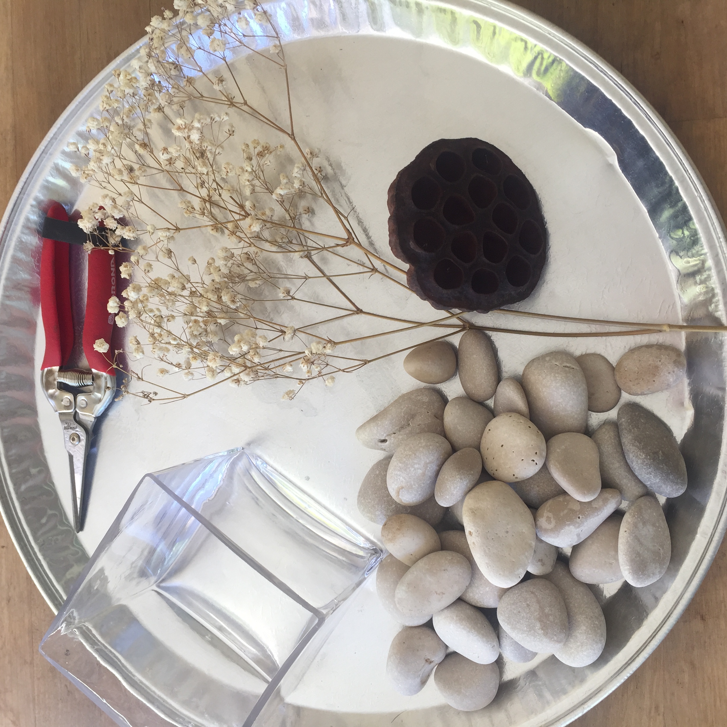 Materiales: recipiente en cristal, piedras pequeñas blancas de 1 a 2 pulgadas; rama de Gypsophila seca (Baby´s Breath); una vaina seca de flor de loto y tijeras.